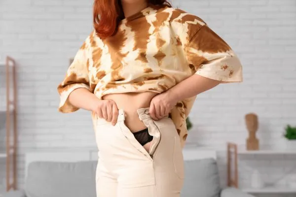 Image of woman trying to do her trousers up after pregnancy weight gain Greenhead